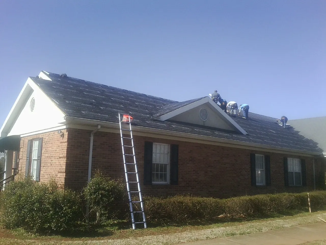 Crew tearing shingles off a brick ranch roof with a ladder set — Metal Roof Repair work by our crew in Rosemount