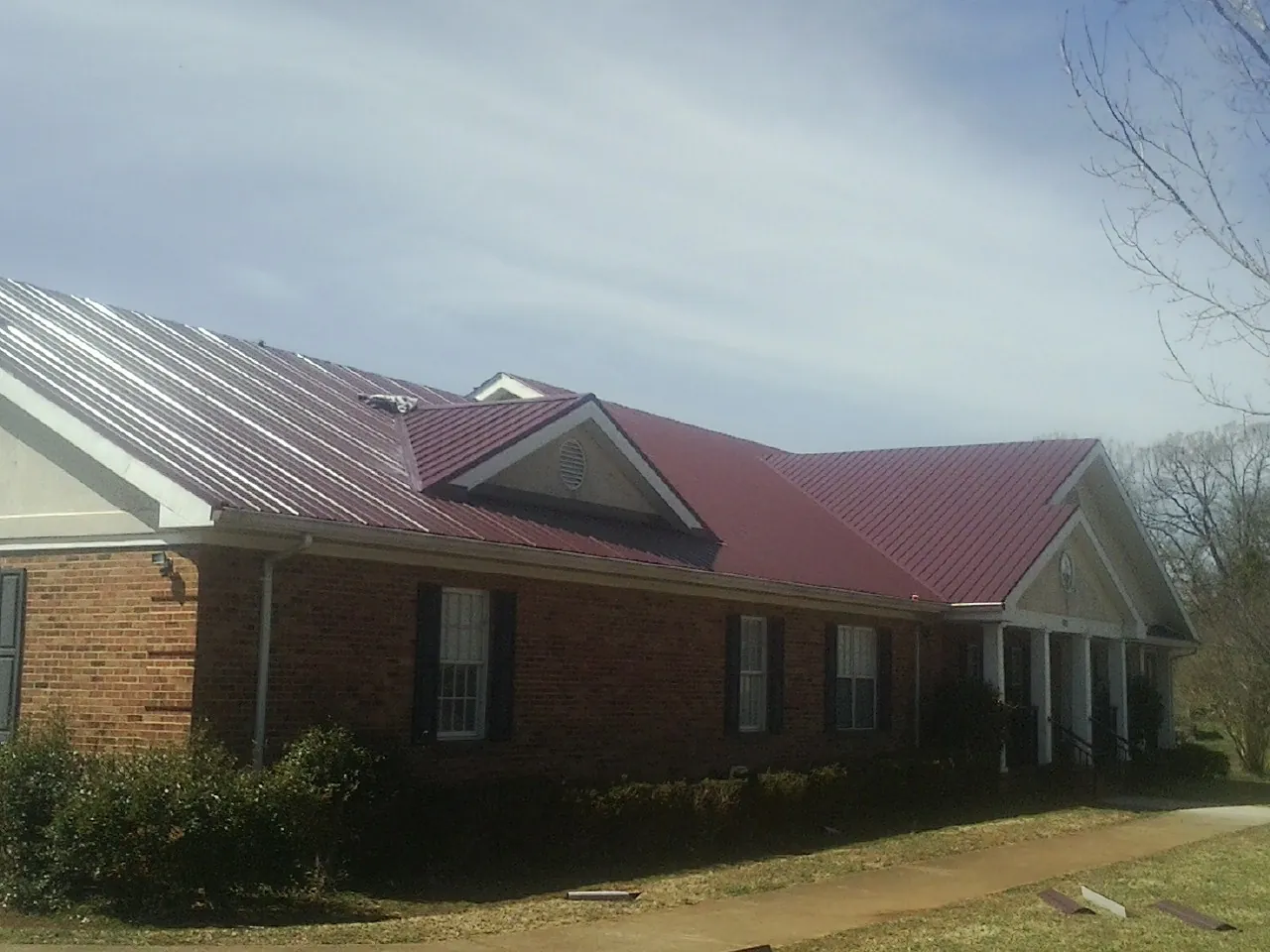 Red metal roof with gabled entries on a long brick building, from a Hail Damage Roof Repair job in Rosemount