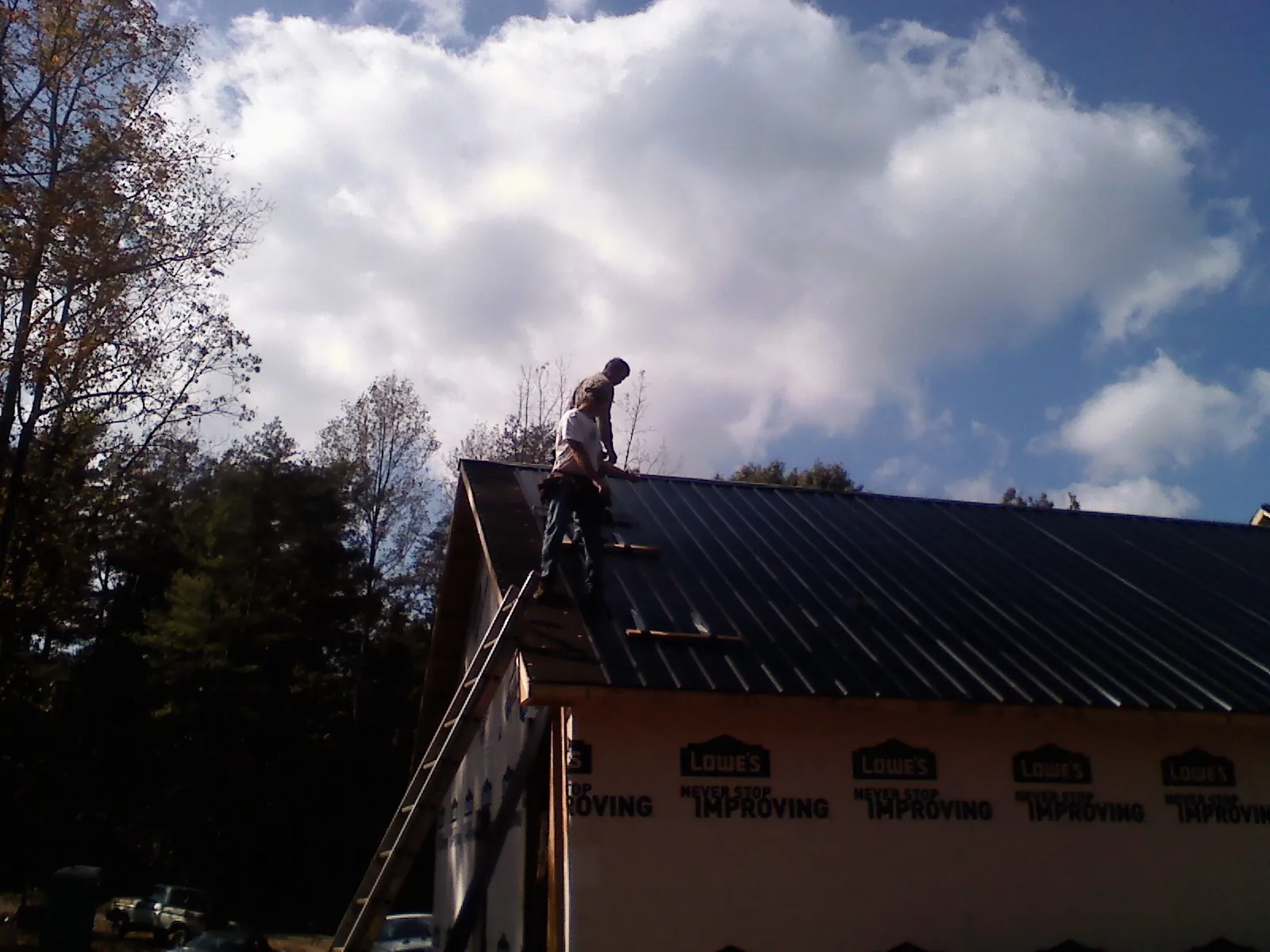 Roofer fastening dark metal panels high against a cloudy sky, from a Roof Inspection job in Rosemount