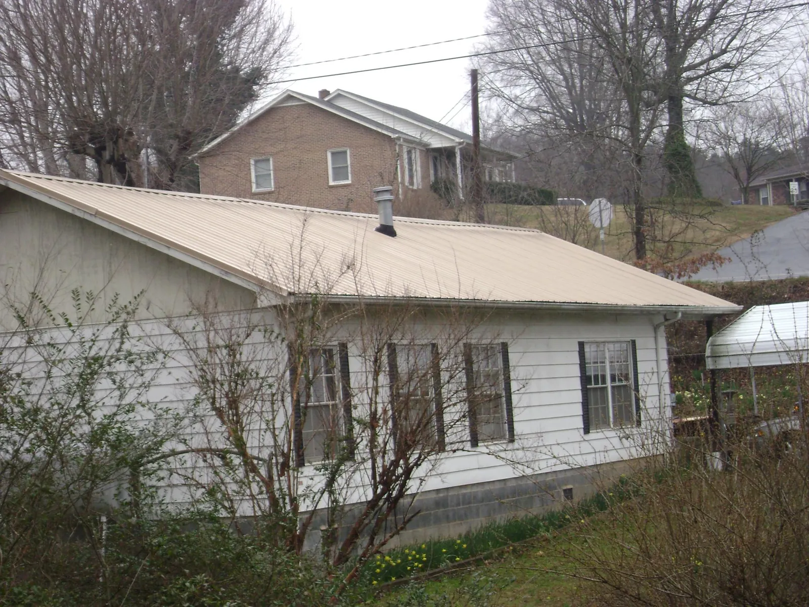 Tan metal roof on a white sided house set into a hillside — Commercial Roofing by Roofing Brothers in Rosemount